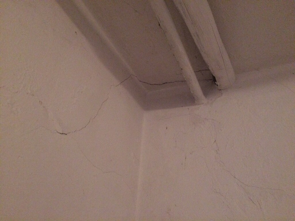 Sichtbare Risse in Wand und Decke eines Kellerraums mit Holzbalken.