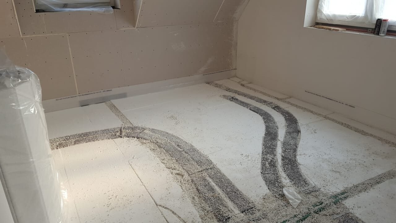 Badezimmer im Rohbau mit verlegten Bodenheizungsrohren im Boden, Staub und unfertigen Wänden.