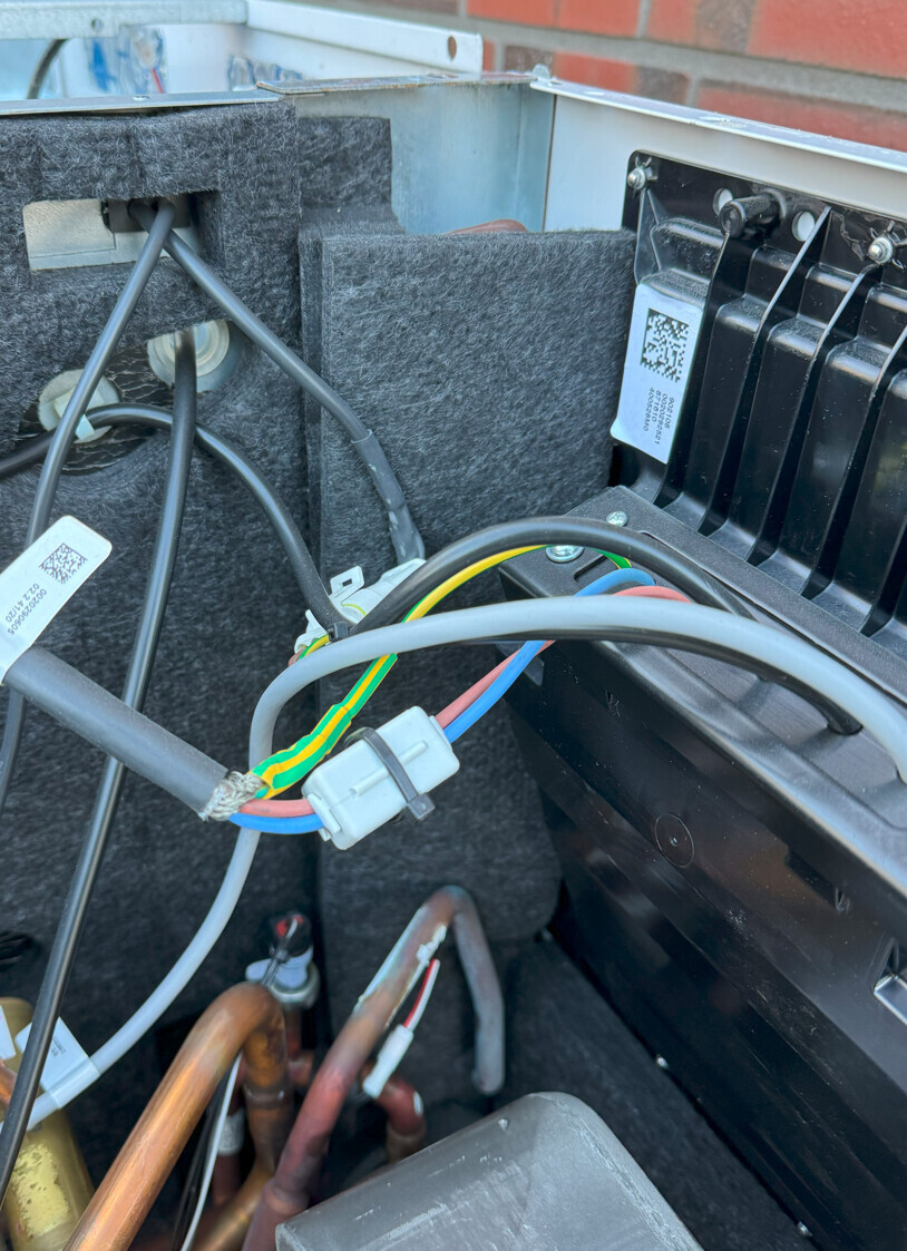 Nahaufnahme von Kabeln, Stecker und Kupferrohren im Innenbereich eines Heiz-/Kühlgeräts.