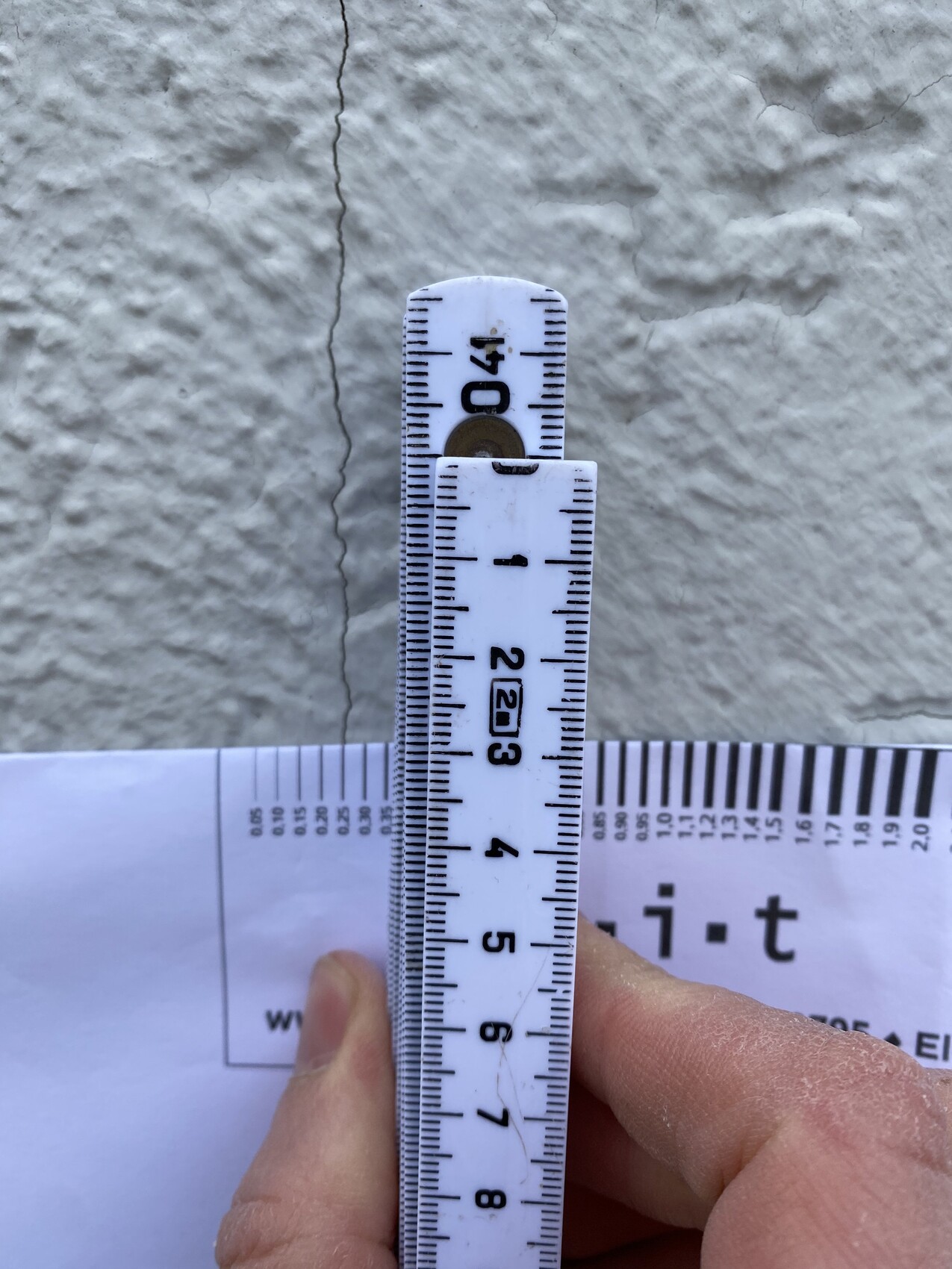 Faltsmaßstab wird von einer Hand senkrecht vor rauer Wand mit Riss gehalten; ca. 40 cm.