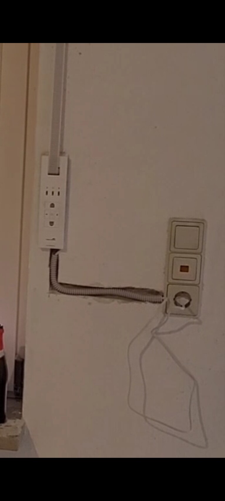 Weißes Mehrfachstecker-Modul an der Wand, flexibles Kabel, daneben zwei quadratische Schalter und runder Knopf.