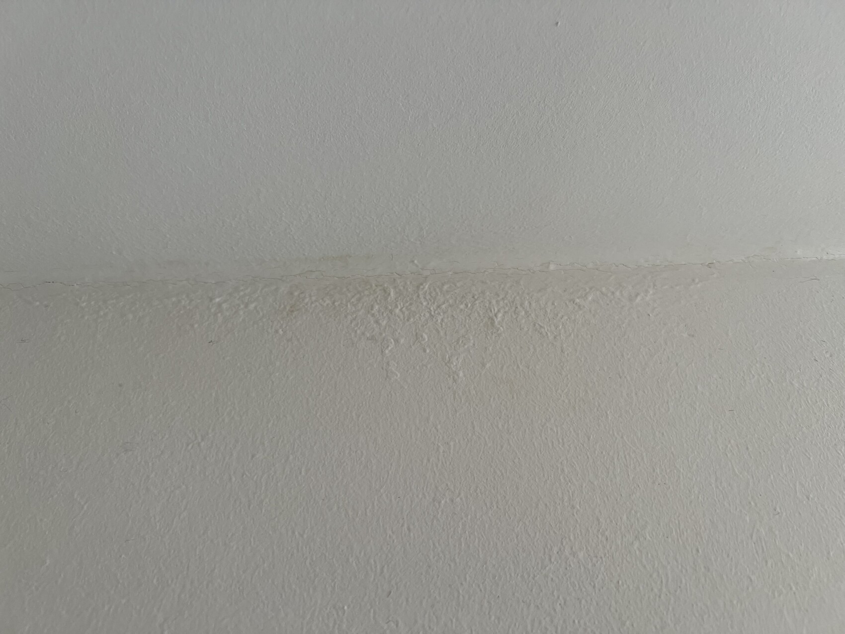 Weiße Wand mit horizontaler Fuge und rauem Putz.