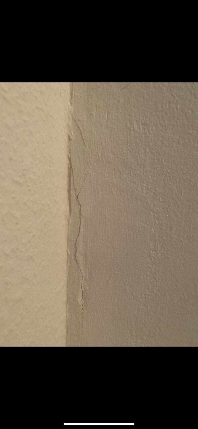 Feiner vertikaler Riss im Putz einer Wand nahe der Ecke, beige Oberfläche.
