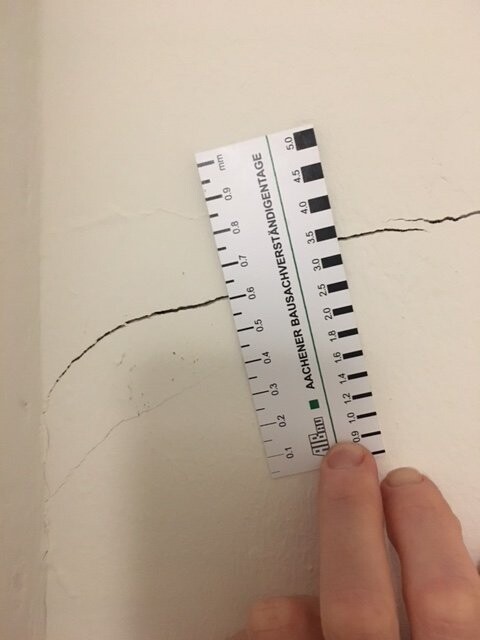 Riss in heller Wand, Messleiste mit Skala wird von einer Hand gehalten.