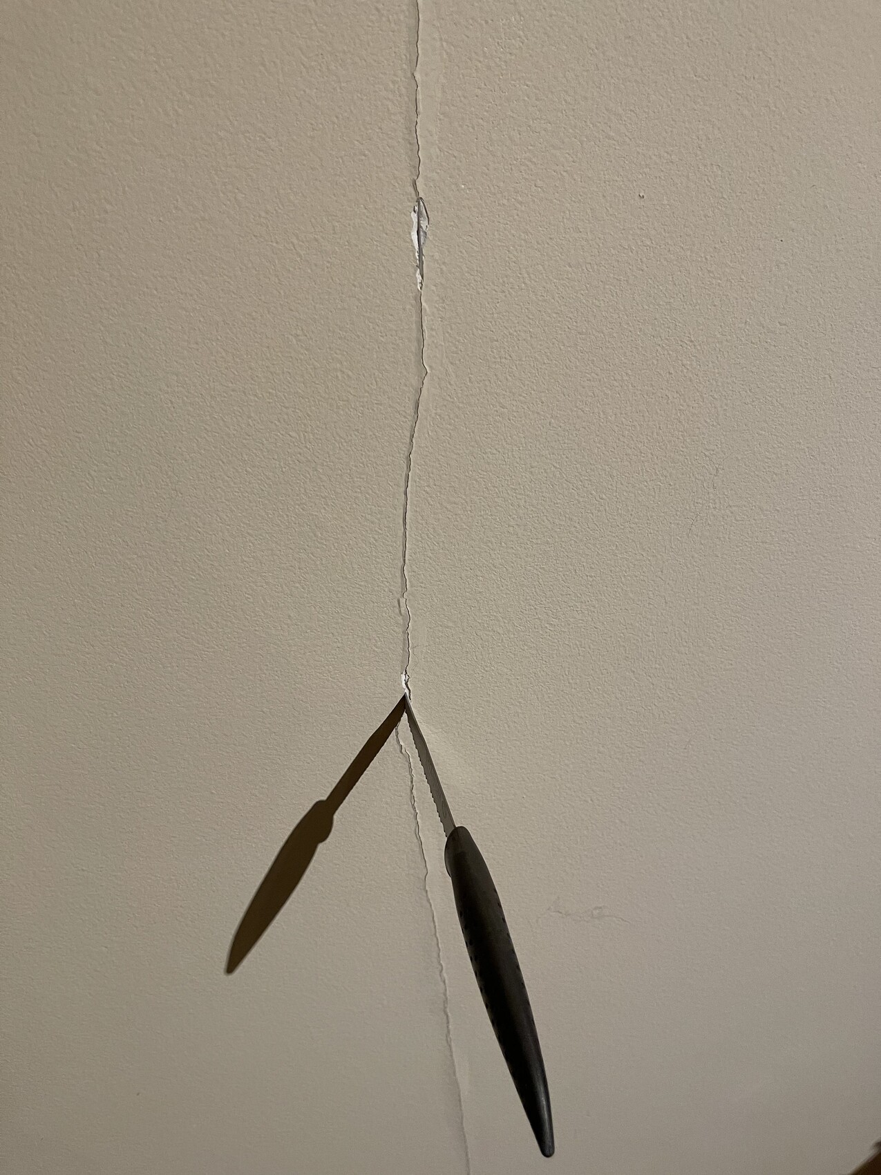 Beige Wand/Decke mit vertikalem Riss; zwei Klingen eines Werkzeugs ragen in die Spalte.