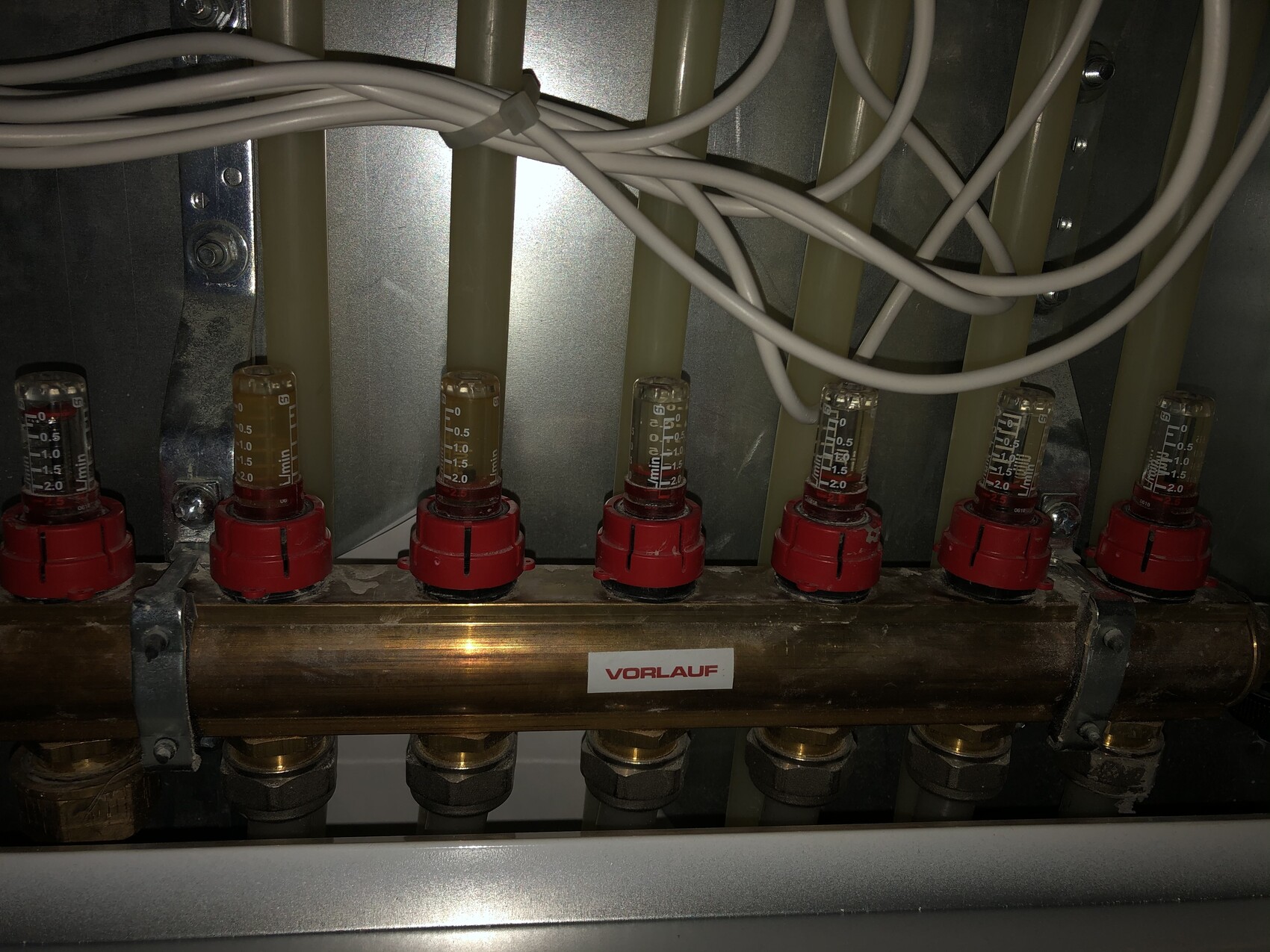 Mehrere Durchflussmesser mit roten Skalen in einer Rohrverteilung, Kabel liegen darüber.