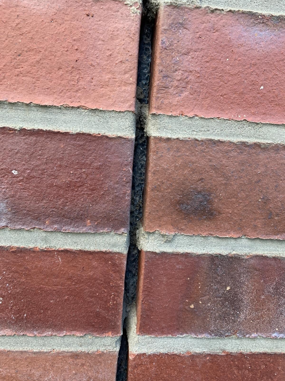 Nahaufnahme roter Backsteinwand mit schmalem Spalt und dunklem Innenraum.