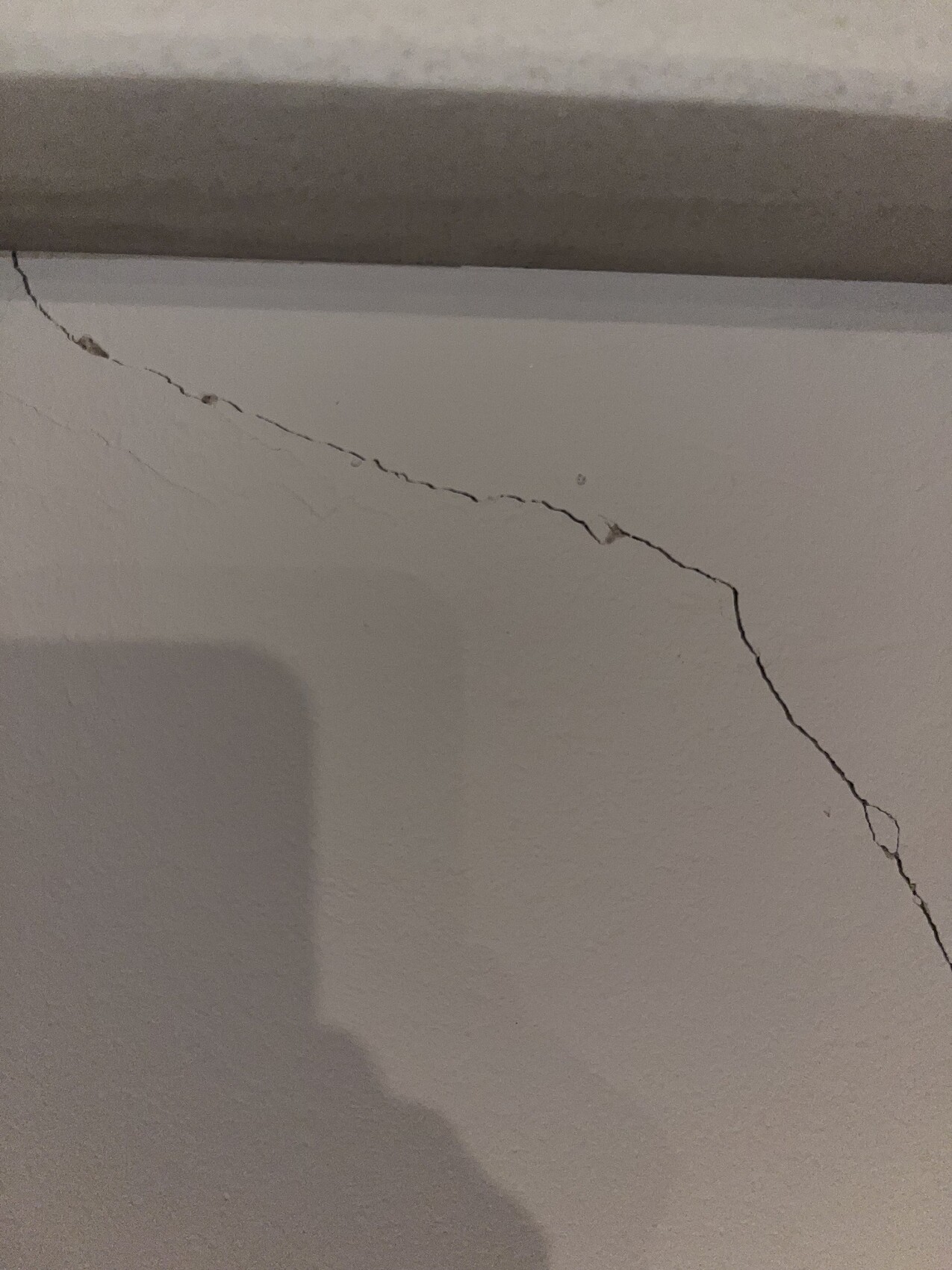 Diagonaler Riss in der Wand nahe der Decke; Schatten einer Person beim Fotografieren.