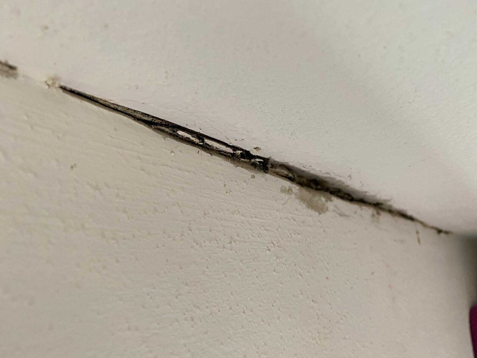 Dünner dunkler Riss verläuft diagonal über eine weiß gestrichene Wand/Decke.