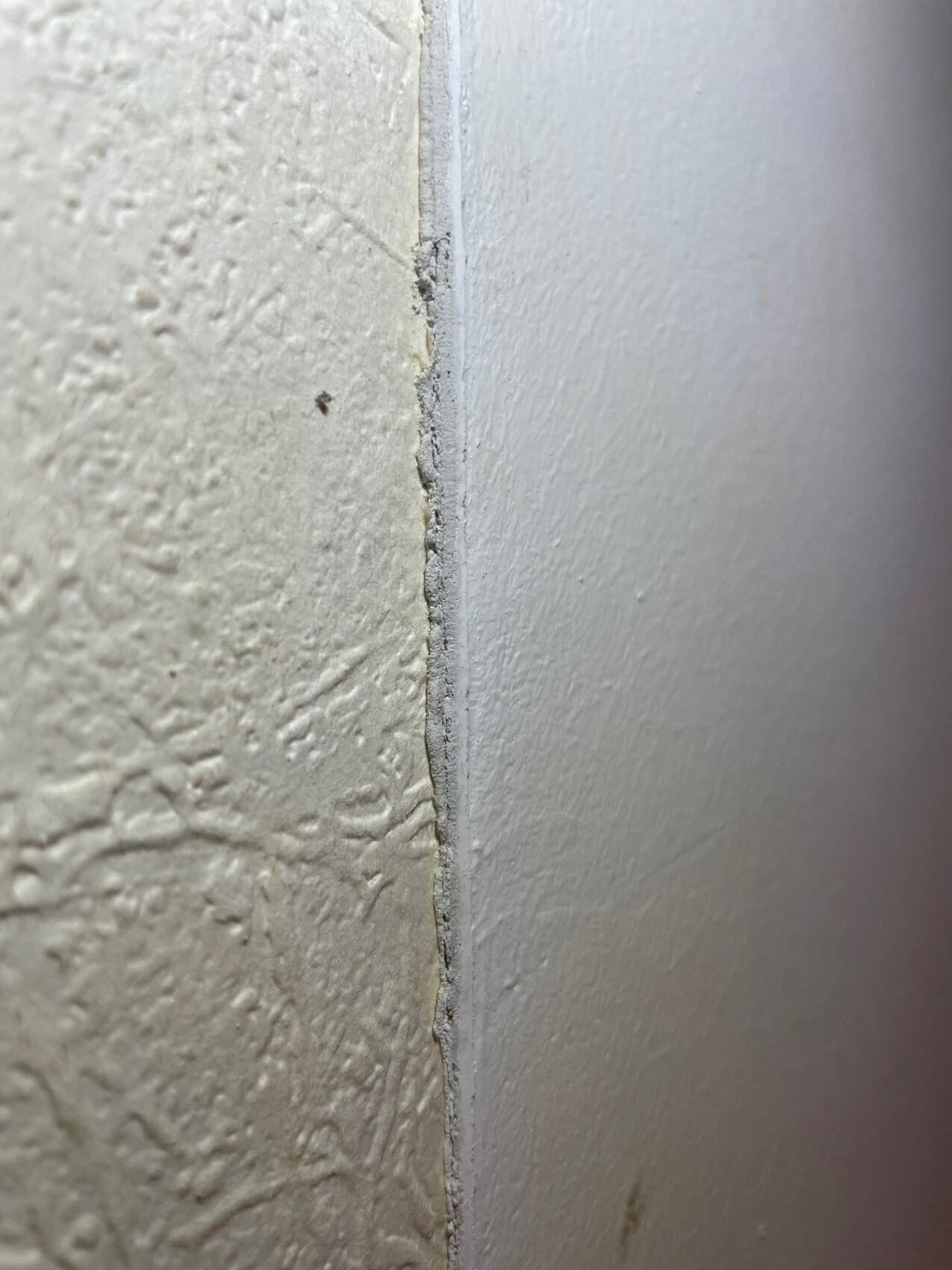 Nahaufnahme einer Eckverbindung: linke beige Wand neben glatte Wand mit Spalt.