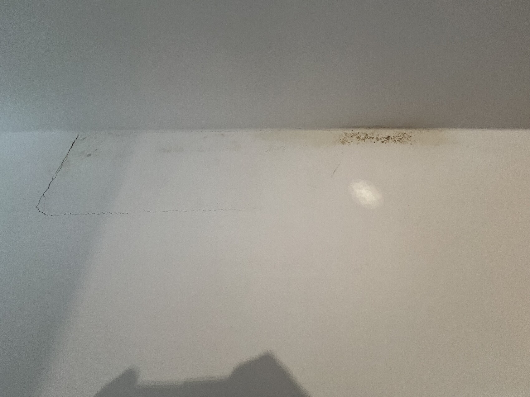 Weiße Wand mit rechteckiger Reparaturfläche, Rissen am Rand und dunklen Flecken.