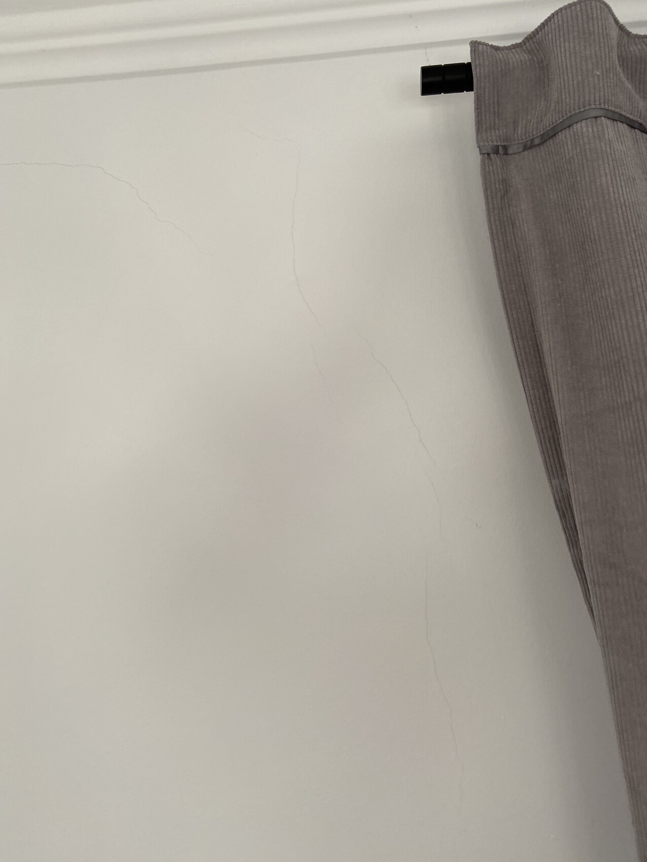 Weiße Wand mit feinen Rissen; grauer Vorhang rechts, Stange oben sichtbar.