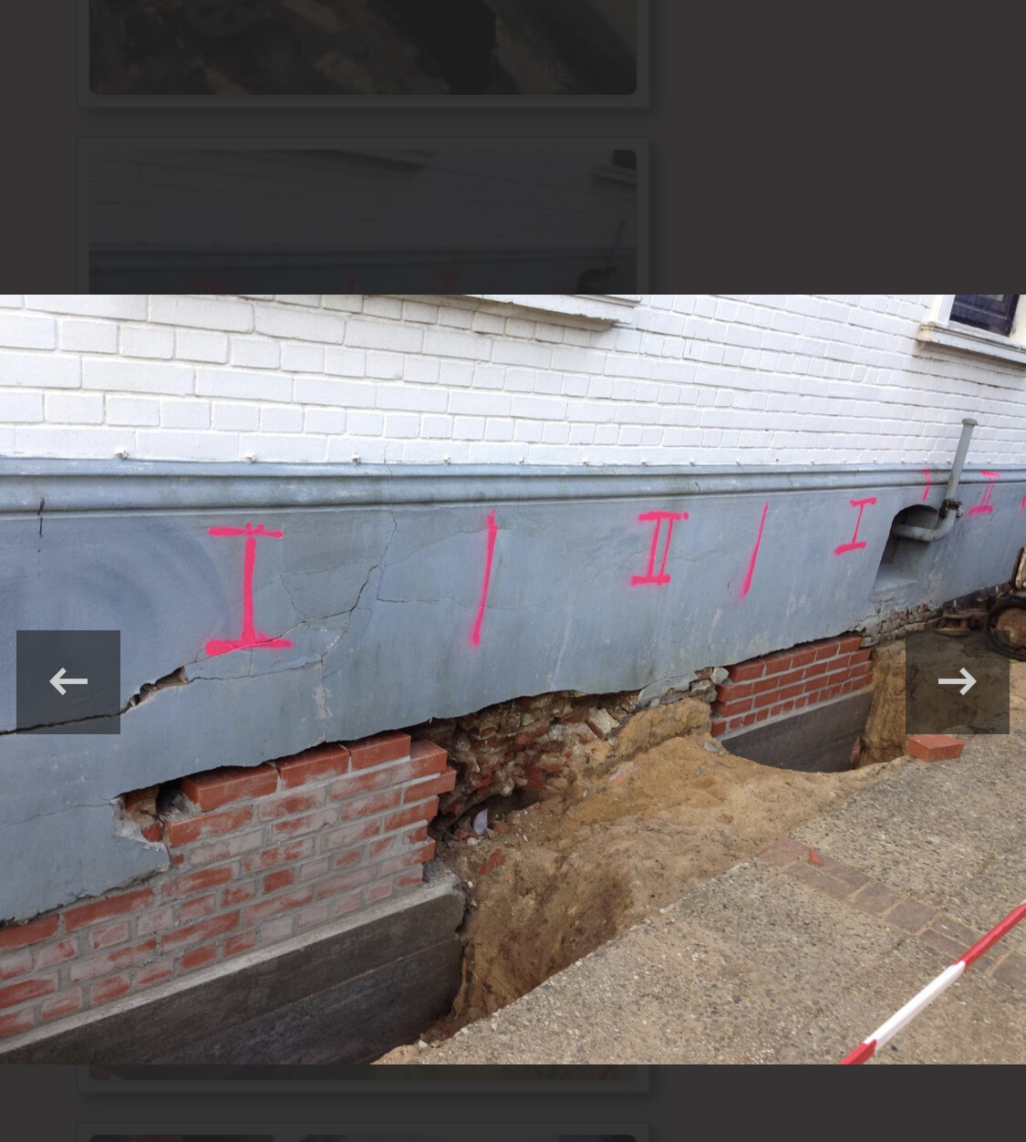 Fundament eines Hauses freigelegt; rosa Markierungen an der Wand, Baugrube neben Gehweg.
