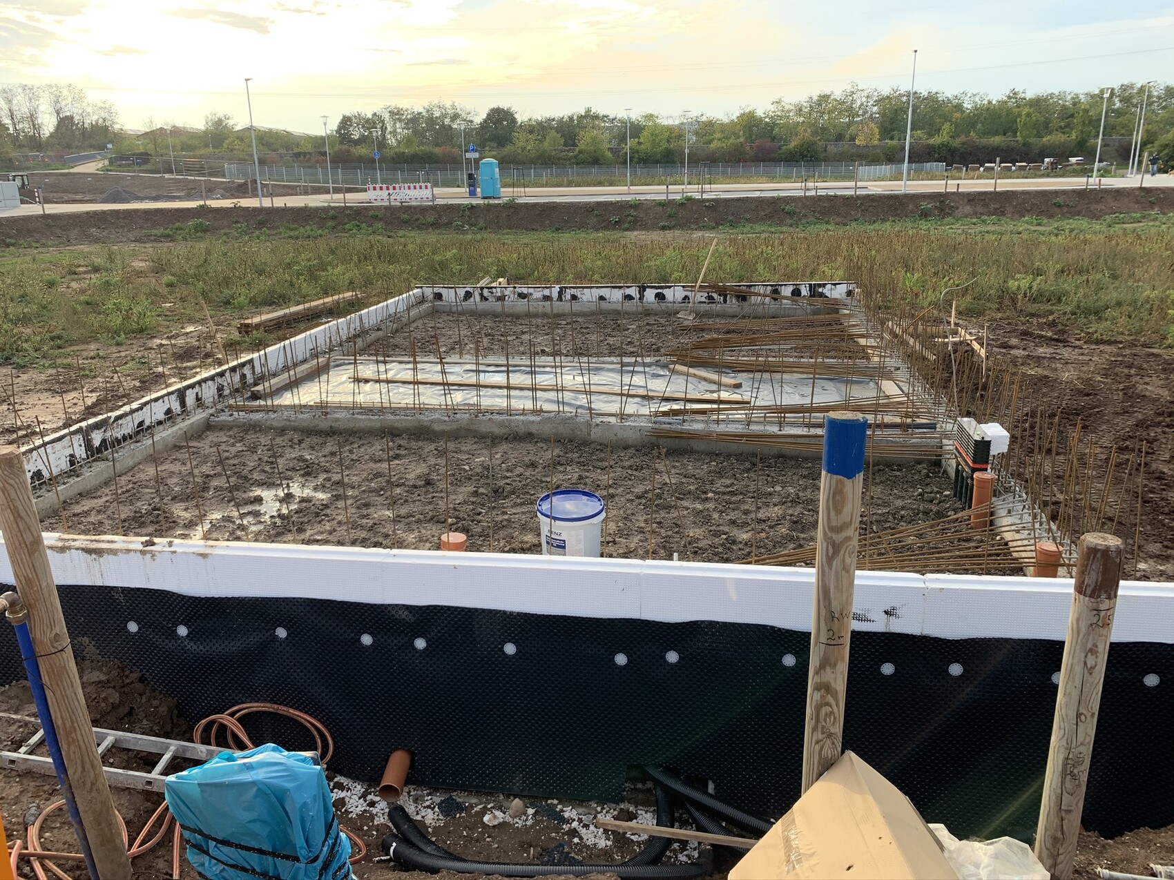Fundament einer Baugrube mit Bewehrungseisen, Dichtungsbahn und Baumaterialien.