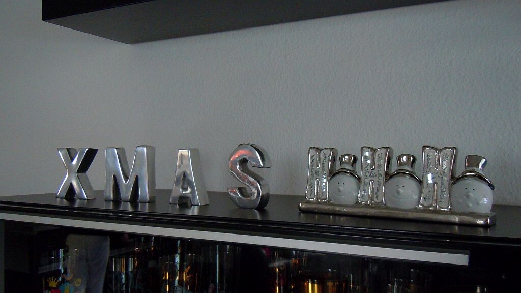 Silberne XMAS-Buchstaben als Deko auf dunkler Holzplatte im Wohnzimmer