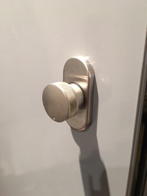 Nahaufnahme eines silbernen Metall-Türknaufs an einer weißen Tür.