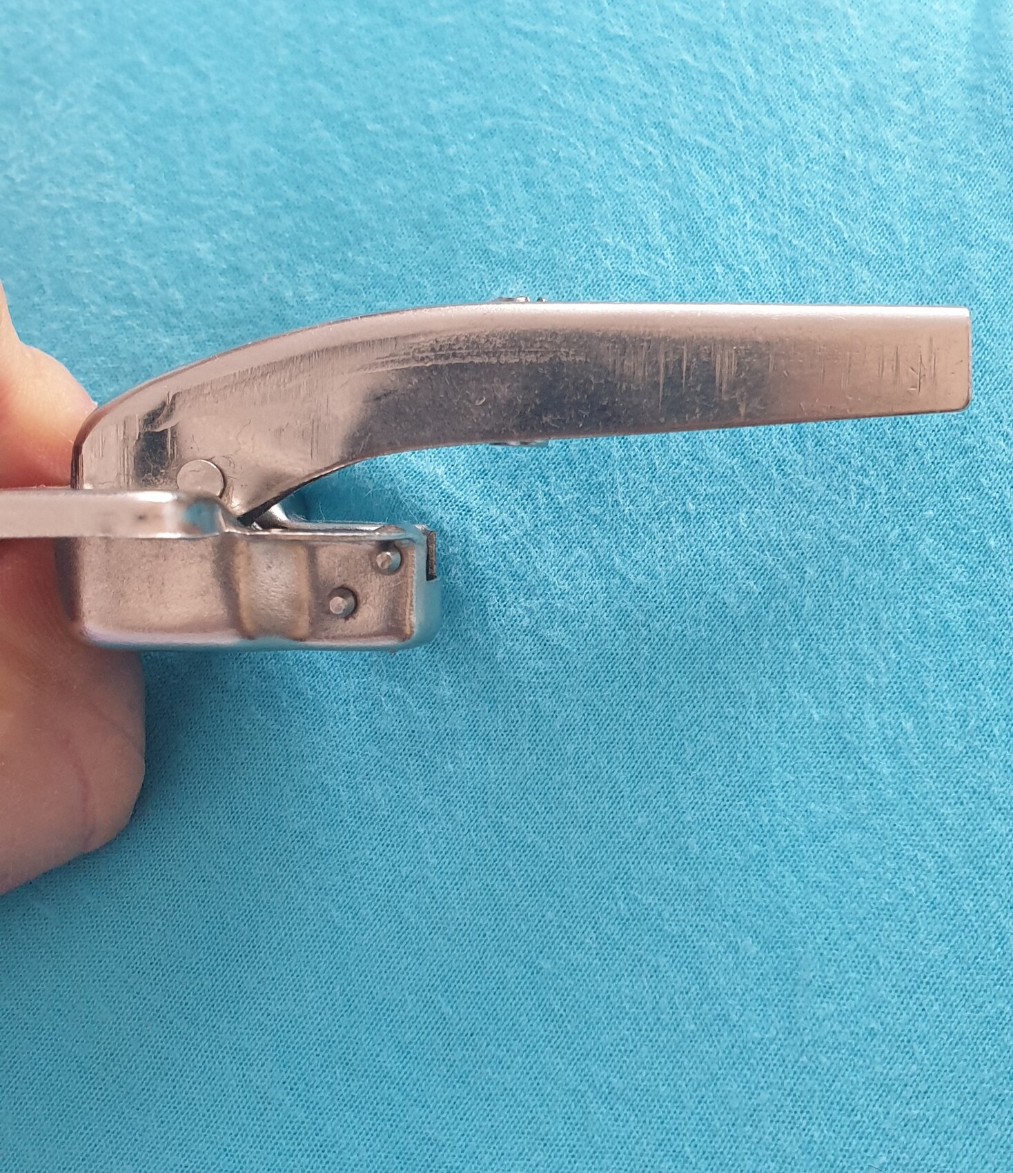 Nahaufnahme eines Metall-Nagelknipsers in der Hand vor blauem Stoff.