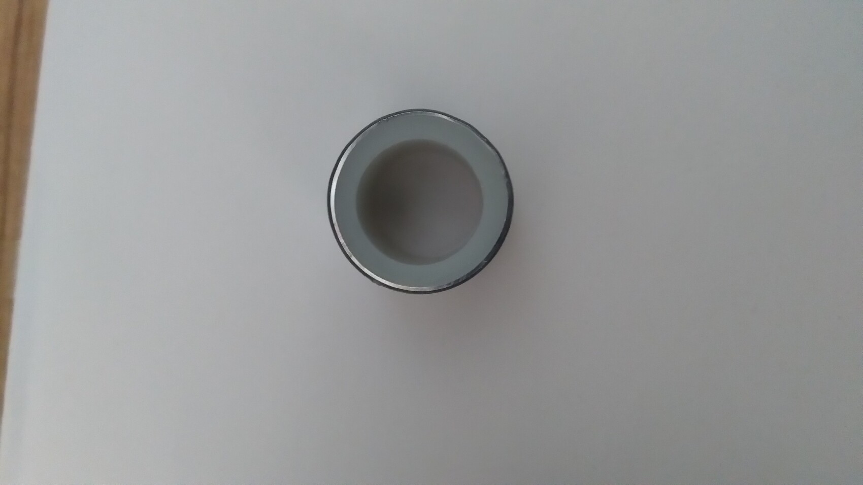 Leerer silberner Metallbecher von oben, runde Öffnung, liegt auf hellem Tisch.