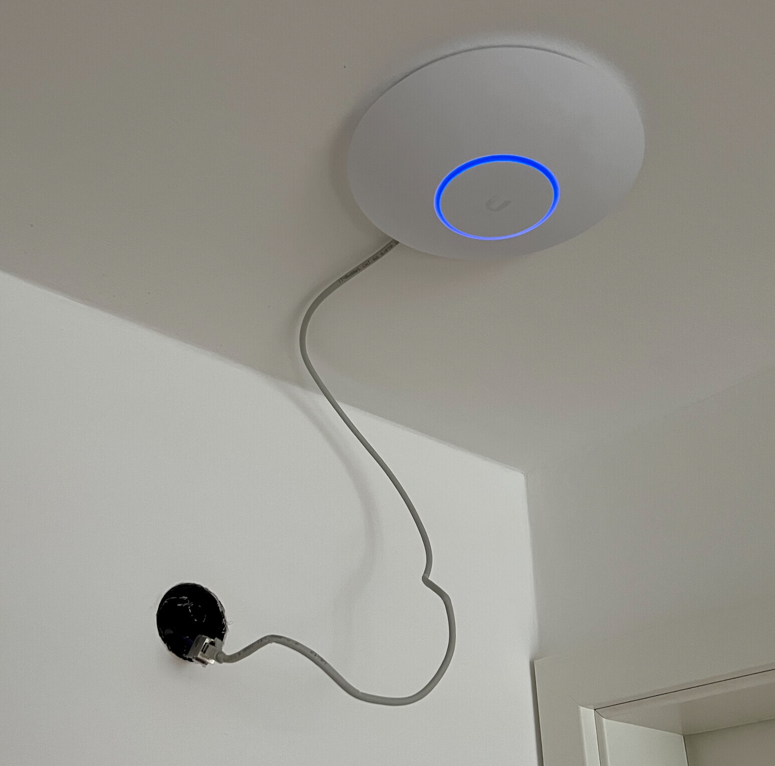 Weiße runde Decken-Einheit mit blauem Ring-Licht; Kabel führt von Gerät zur Wandsteckdose.