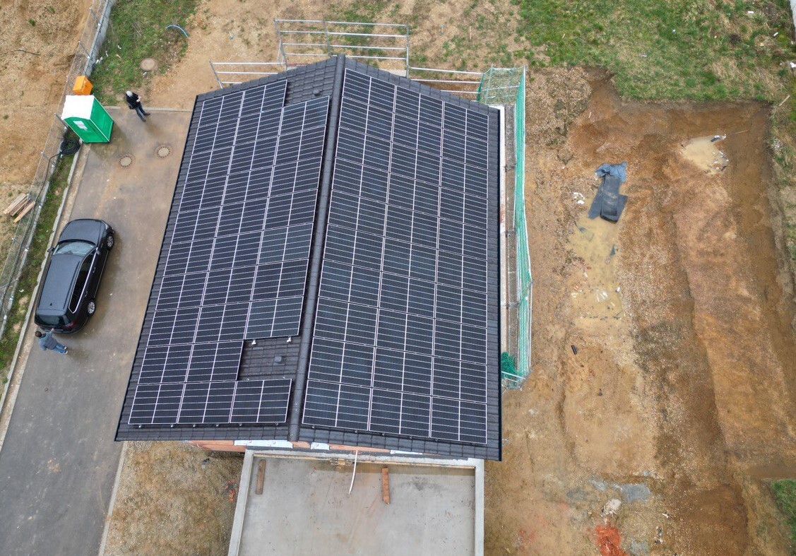 Drohnenaufnahme eines Hauses mit Solarmodulen auf dem Dach; angrenzende Baustelle.