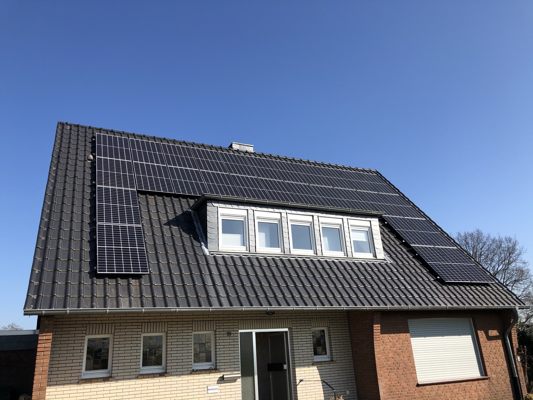 Einfamilienhaus mit Solarpanel-Dach, Dachgaube mit drei Fenstern, blauer Himmel