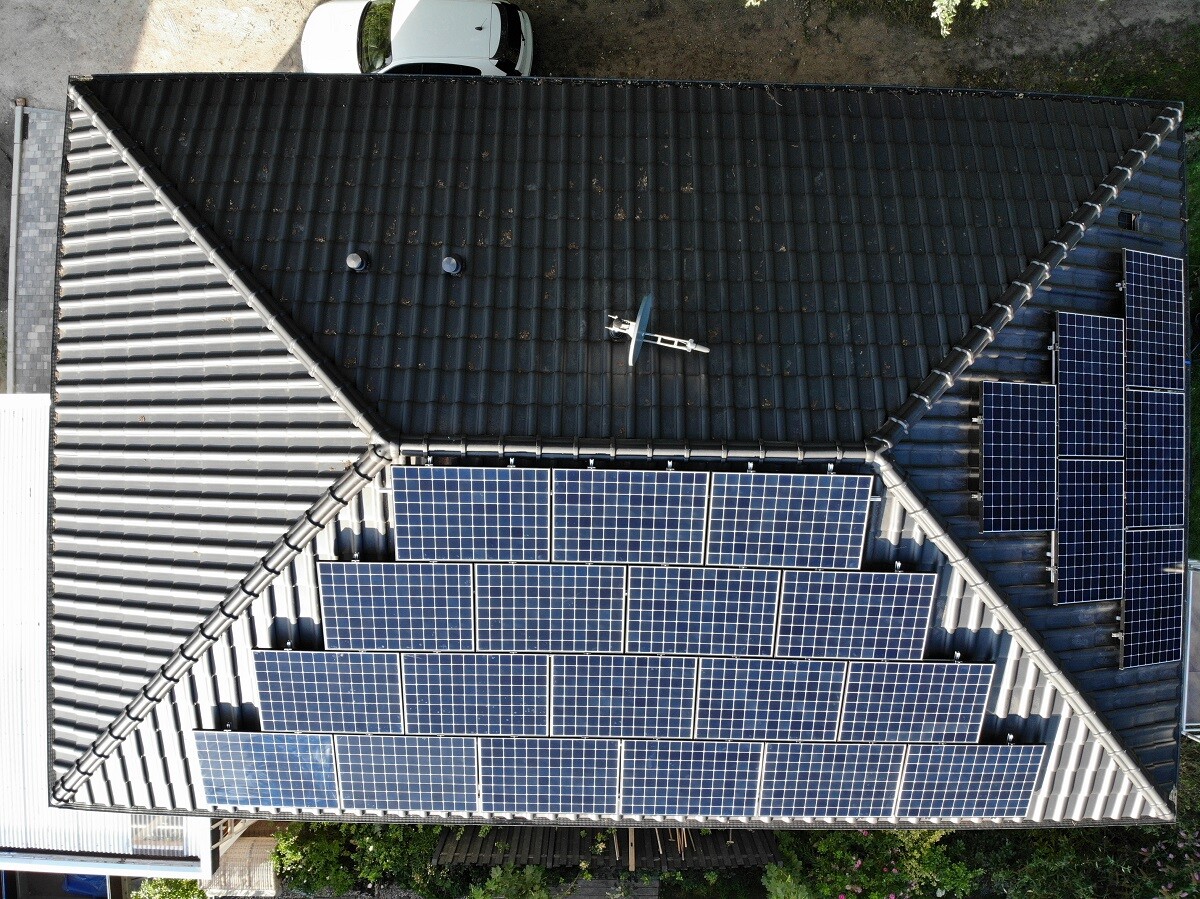 Drohnenaufnahme eines Hausdaches mit vielen blauen Solarpaneelen und einer Satellitenschüssel.