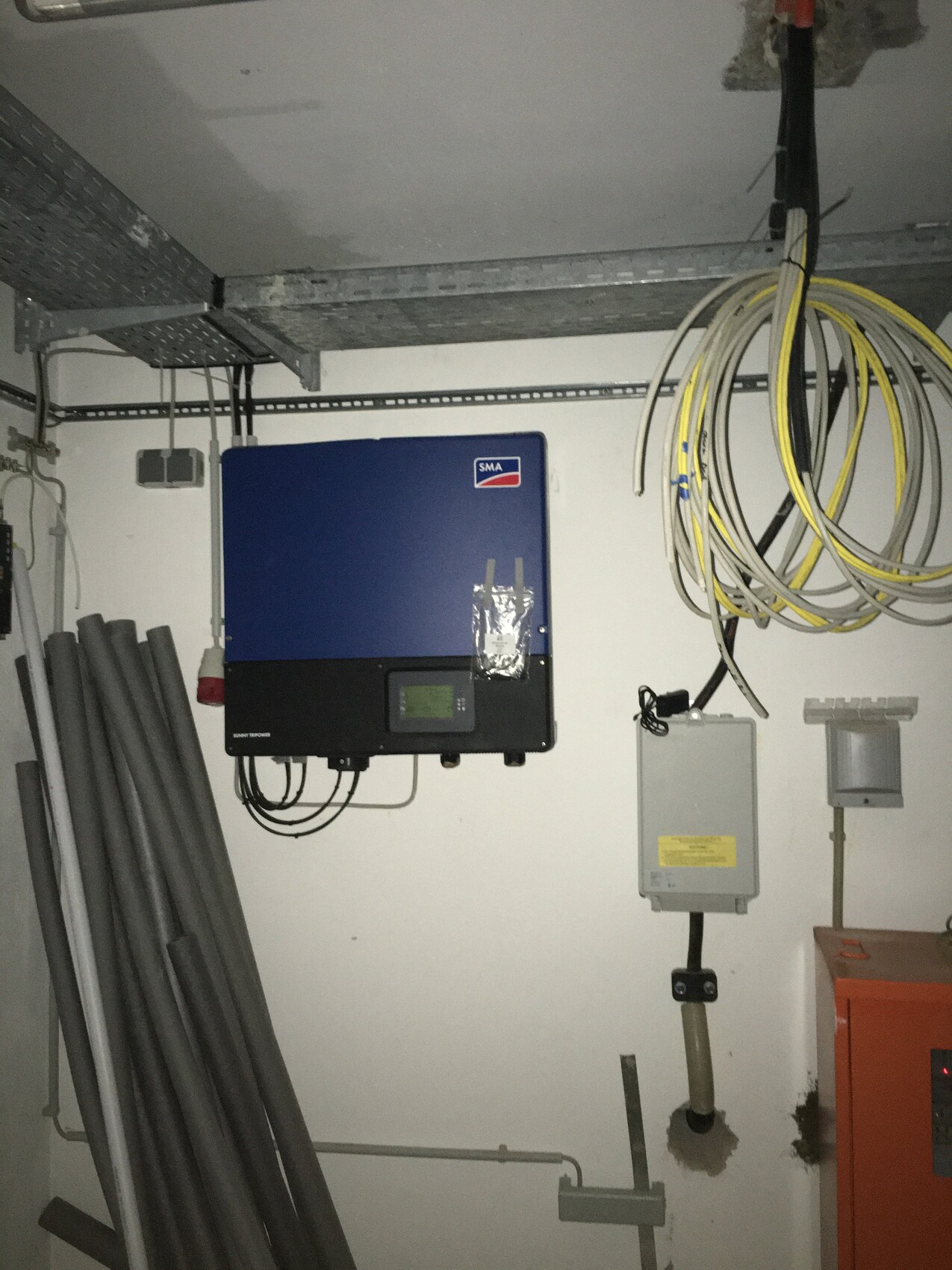 Blaue SMA-Wechselrichteranlage an der Wand; Kabelrollen und Rohre im Technikraum.