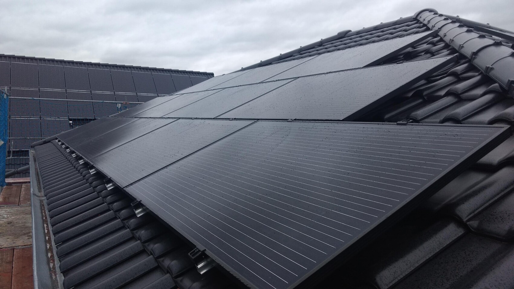 Dach mit dunklen Solarmodulen; nasse PV-Anlage, schräg installiert, Wolkenhimmel im Hintergrund