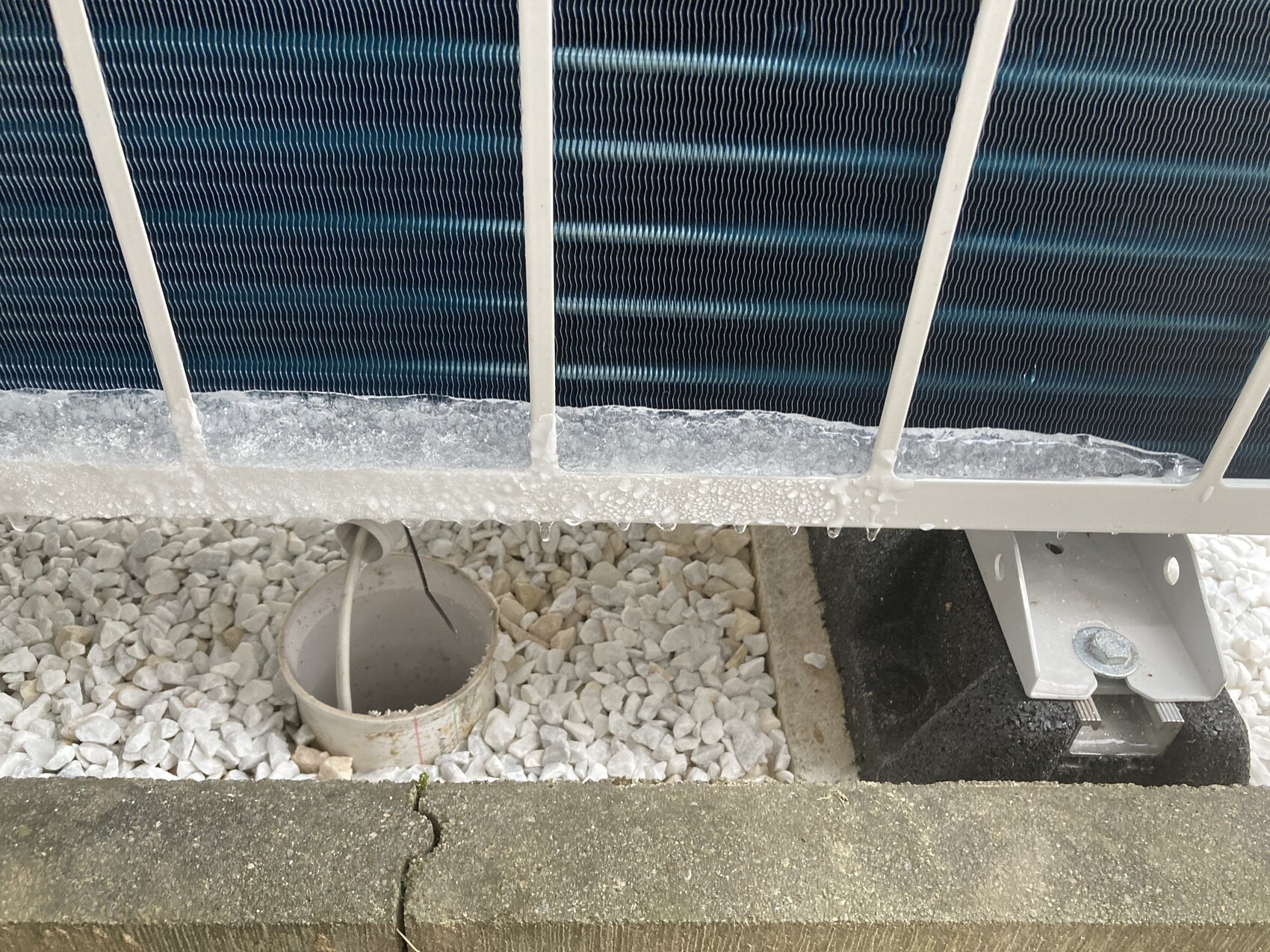 Blaues Flachkollektor-Solarpanel mit Metallrahmen, auf Kiesboden; Rohr führt zu Eimer.