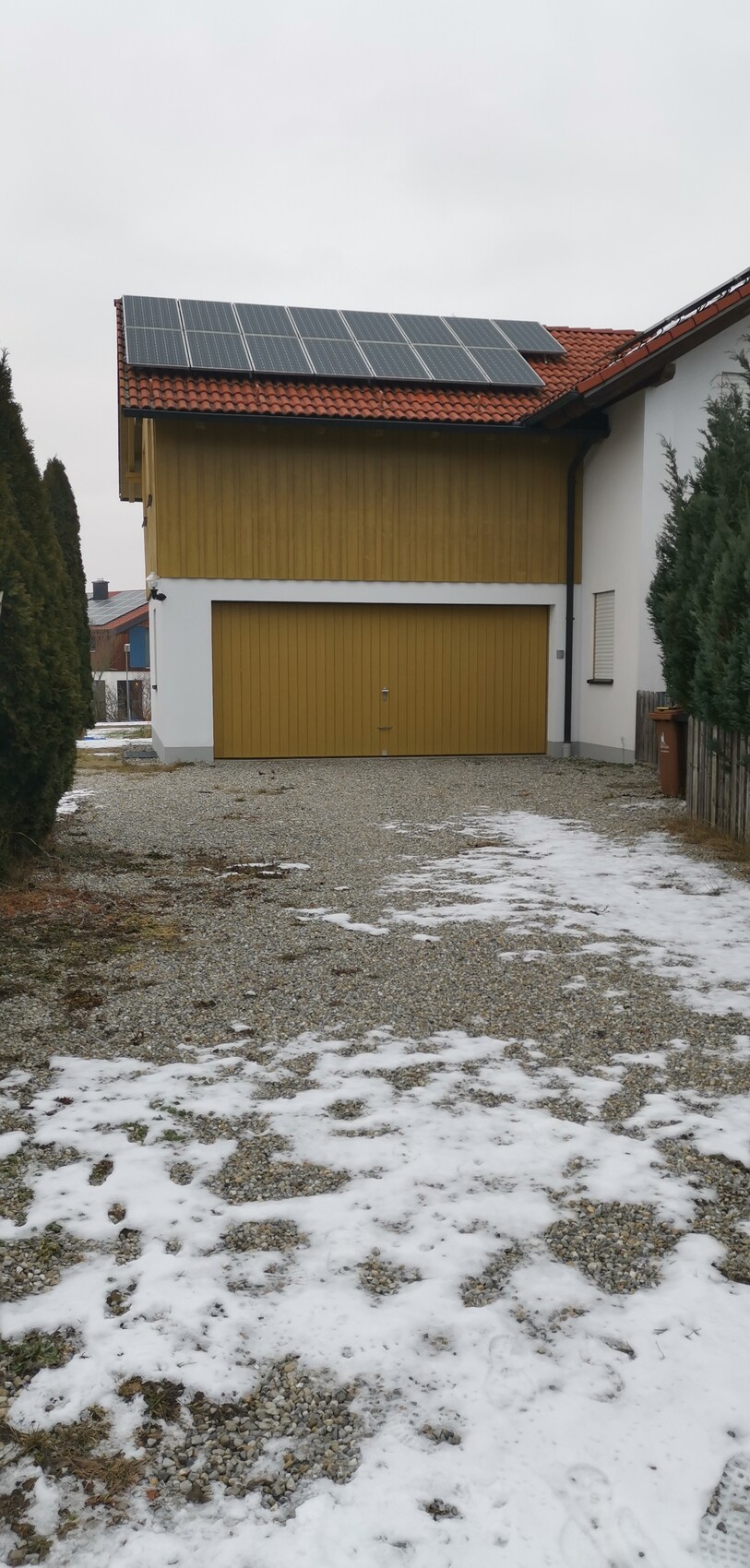 Zweistöckiges Haus mit Holzfassade, Garage und Solarzellen auf dem Ziegeldach, Kiesweg mit Schnee.