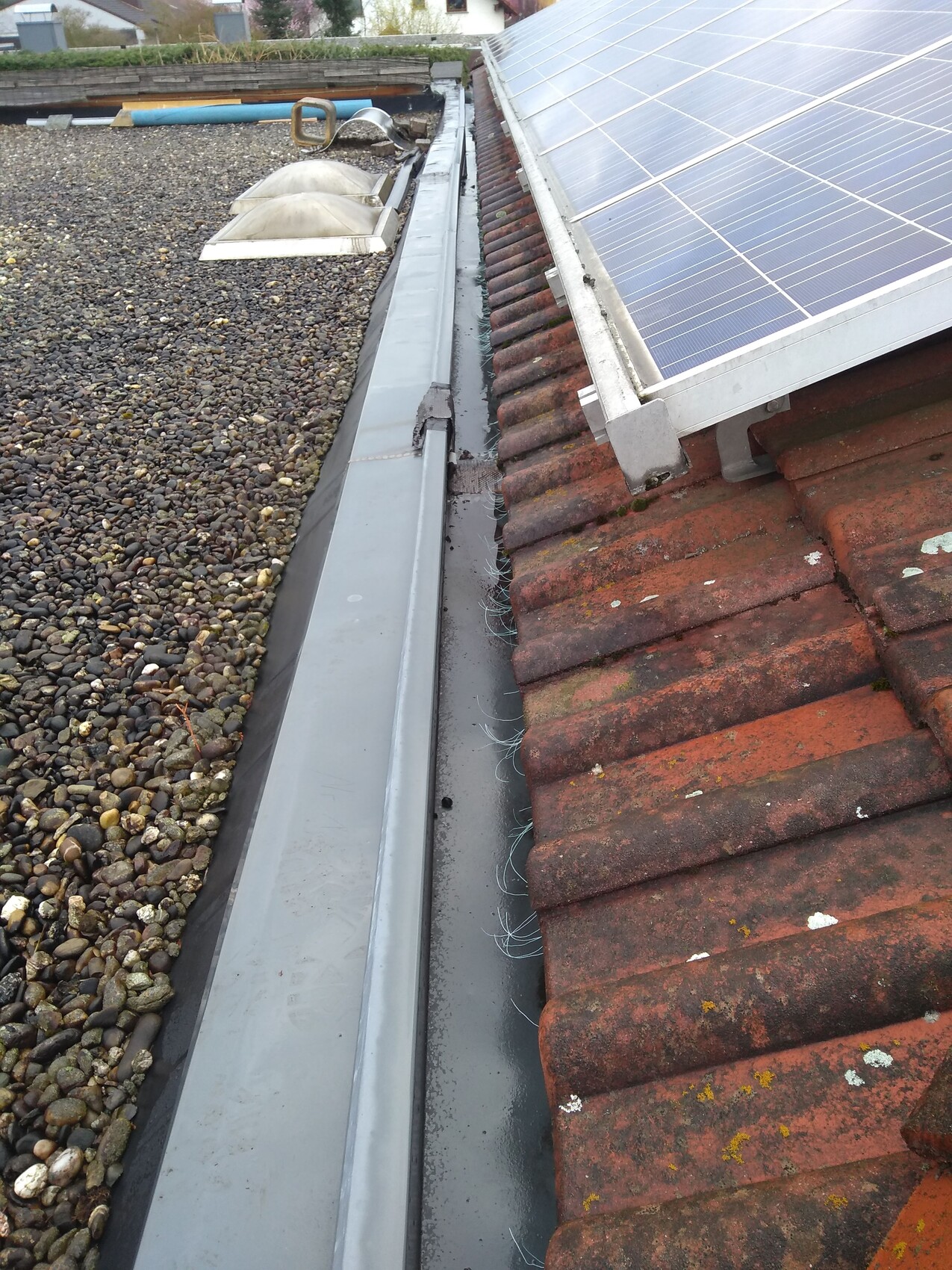 Dach mit installierten solarpanels, Regenrinne und rotem Ziegeldach neben Kiesdach