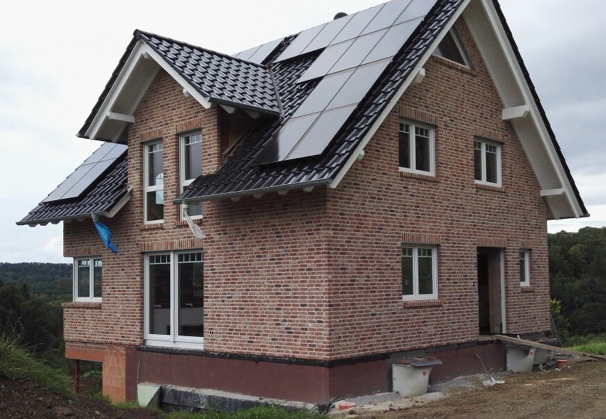 Einfamilienhaus aus Backstein mit Solarmodulen auf dem Dach, Baustelle im Grünen.