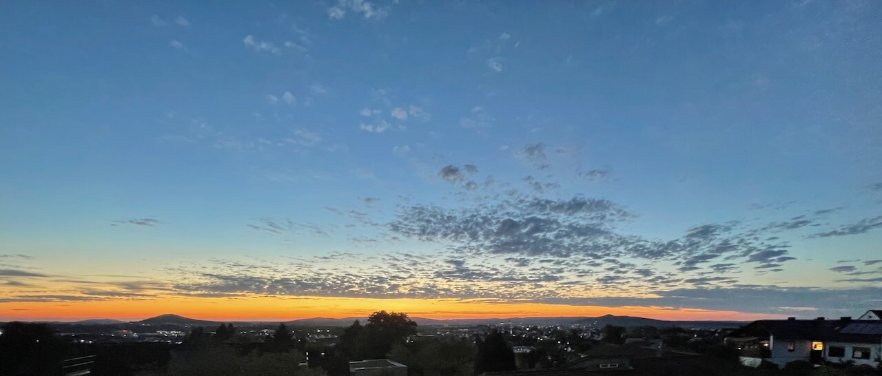 Sonnenuntergang über Stadtlandschaft mit Dächern am Horizont