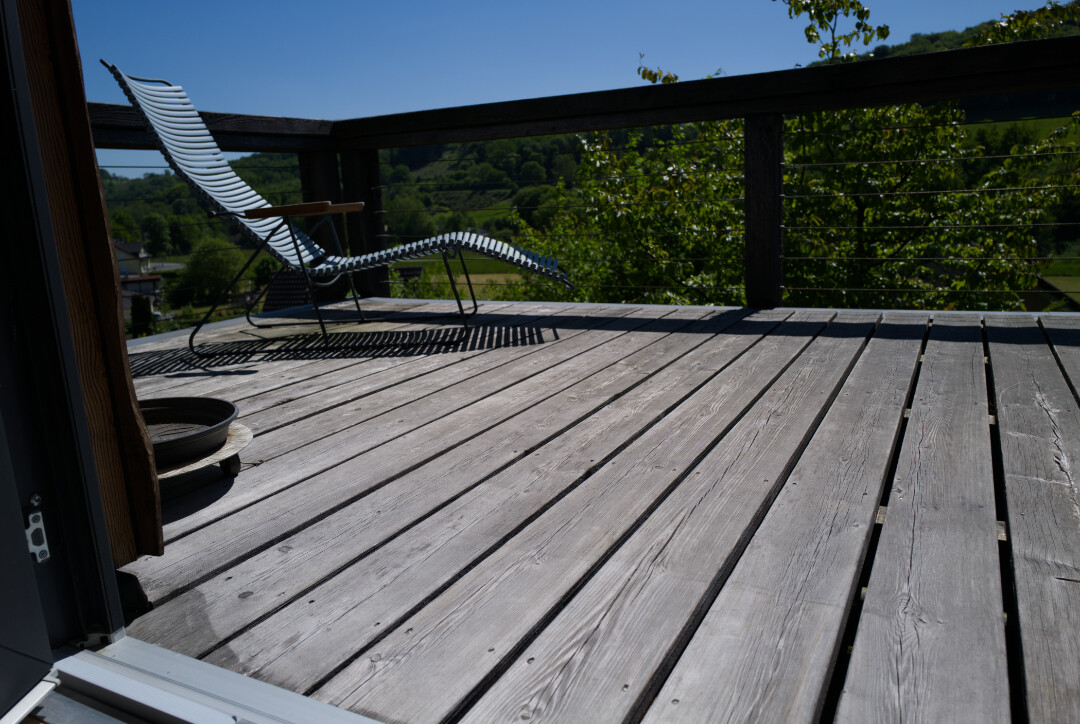 Holzdeck mit Lounge-Stuhl am Geländer; grüne Landschaft und blauer Himmel