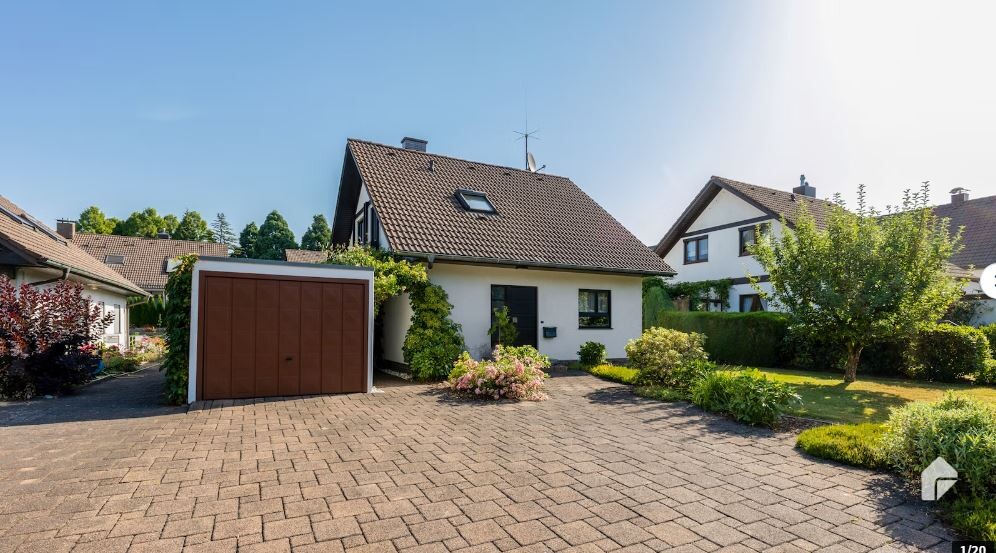 Ein Einfamilienhaus mit braunem Garagen-Tor, gepflasterter Einfahrt und gepflegtem Garten.