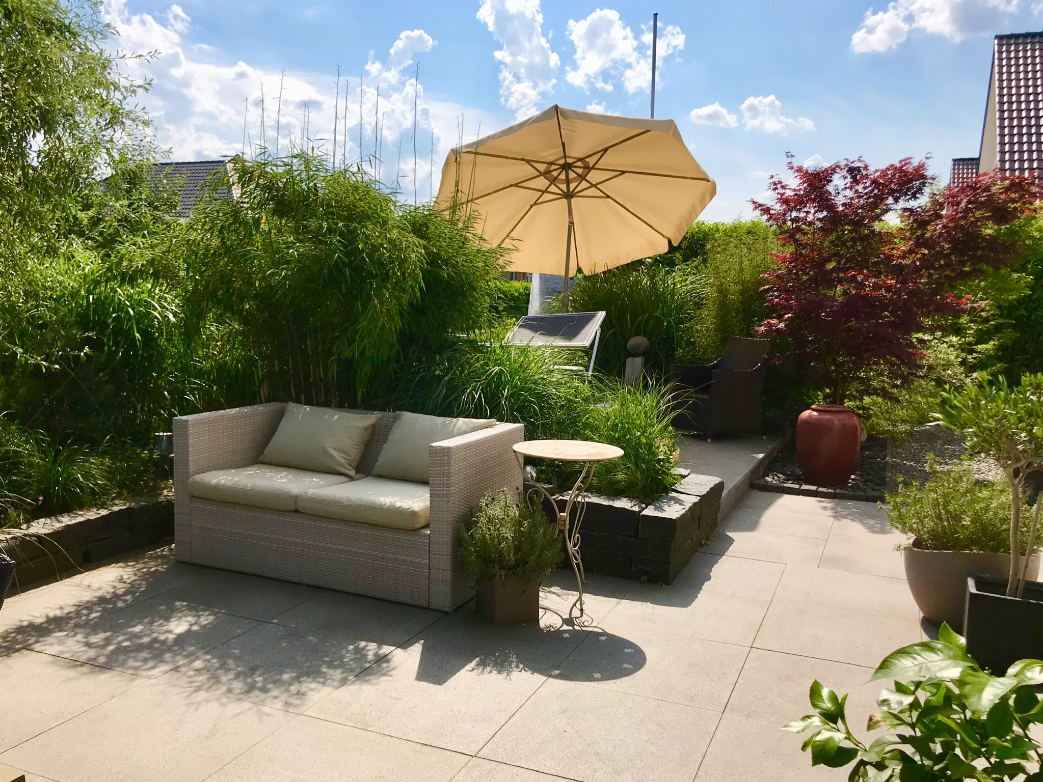 sonnige-terrasse-garten-mobiliar-lounge-sofa-parasol-und-gruenpflanzen-entspannte-atmosphaere.jpeg