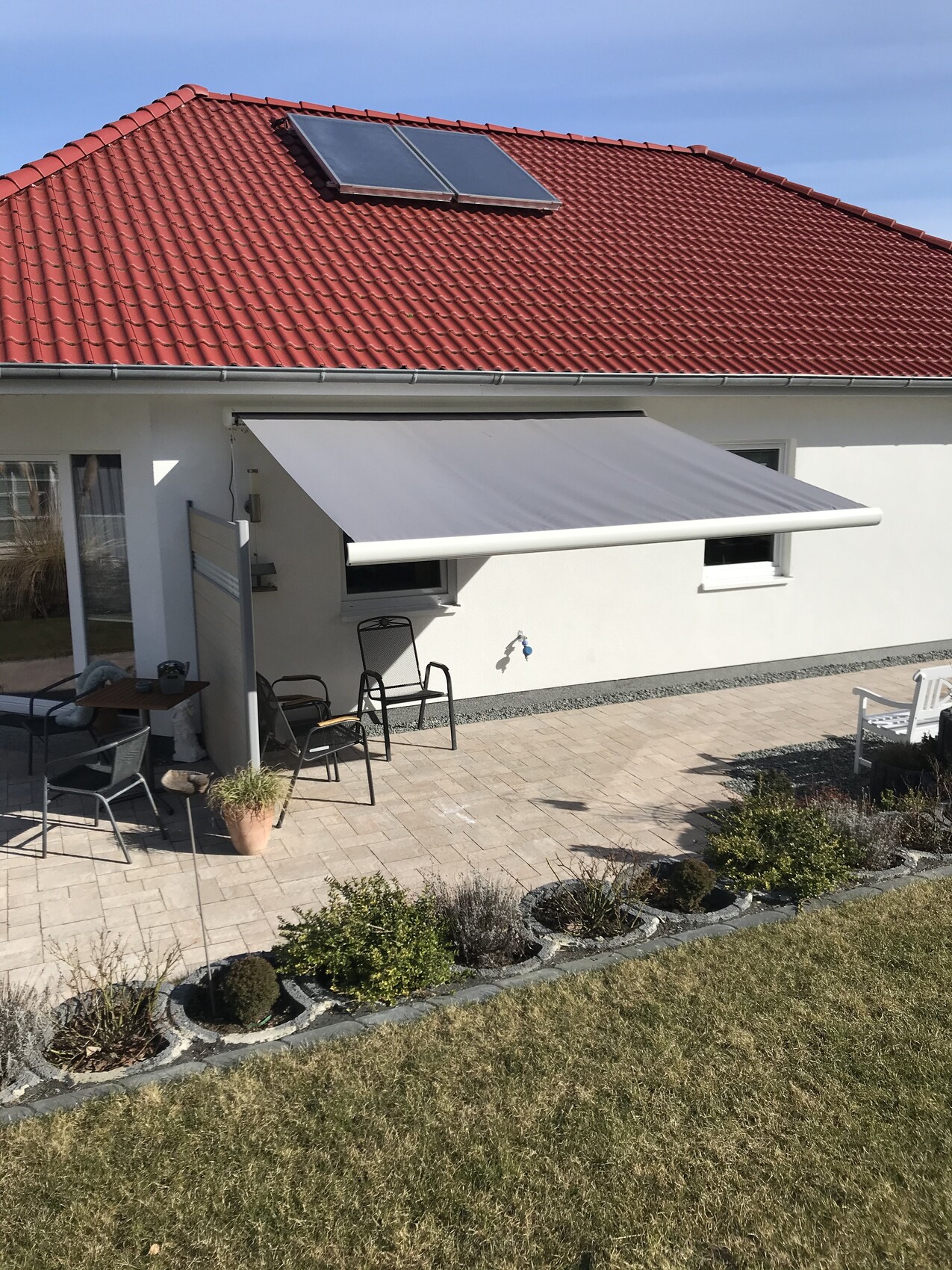 Haus mit rotem Ziegeldach, Solarpanel, ausziehbare Markise über Terrasse, Gartenmöbel