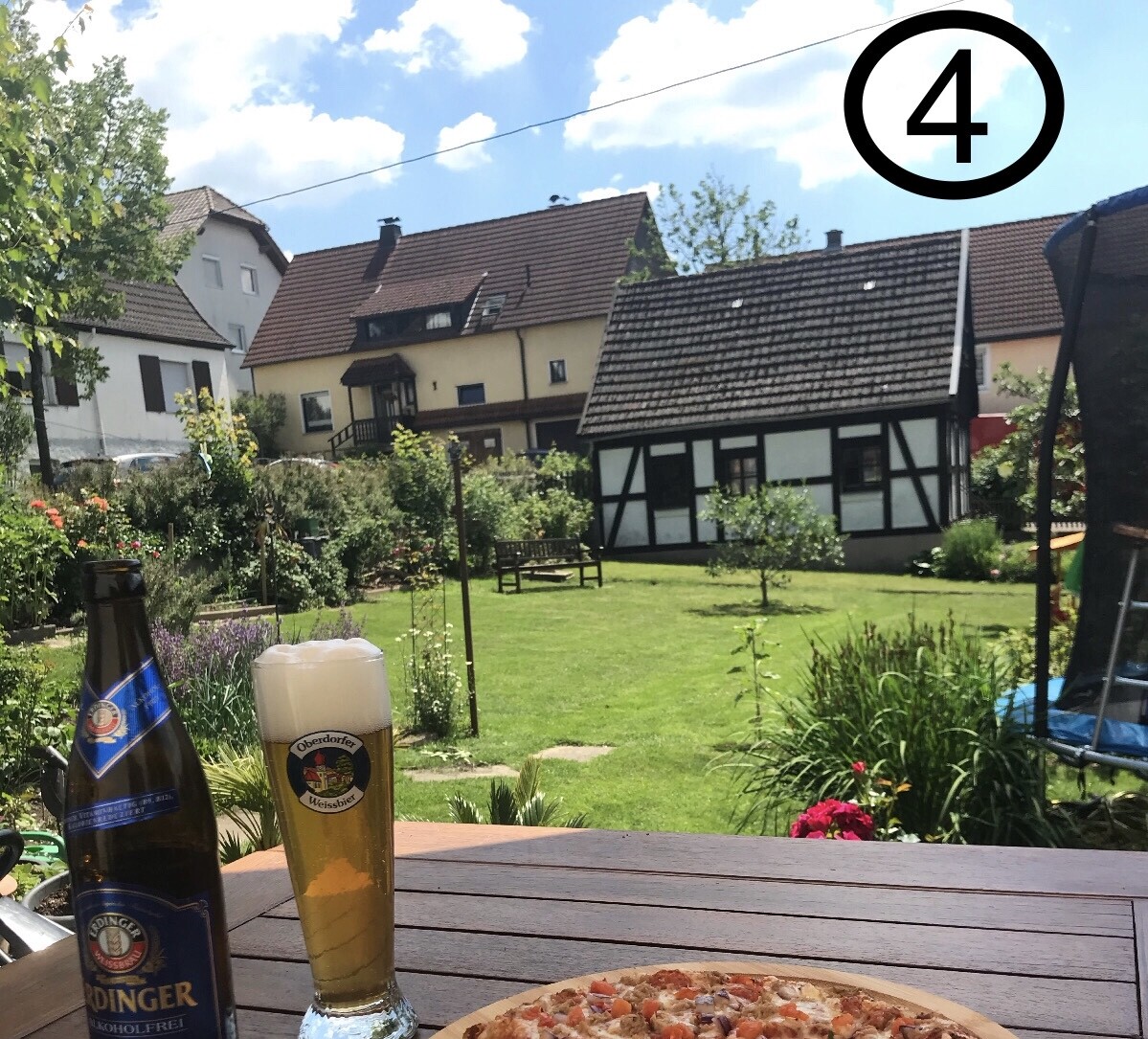 Garten im Ortskern mit Fachwerkhaus, Bierglas, Flasche und Pizza auf Tisch.