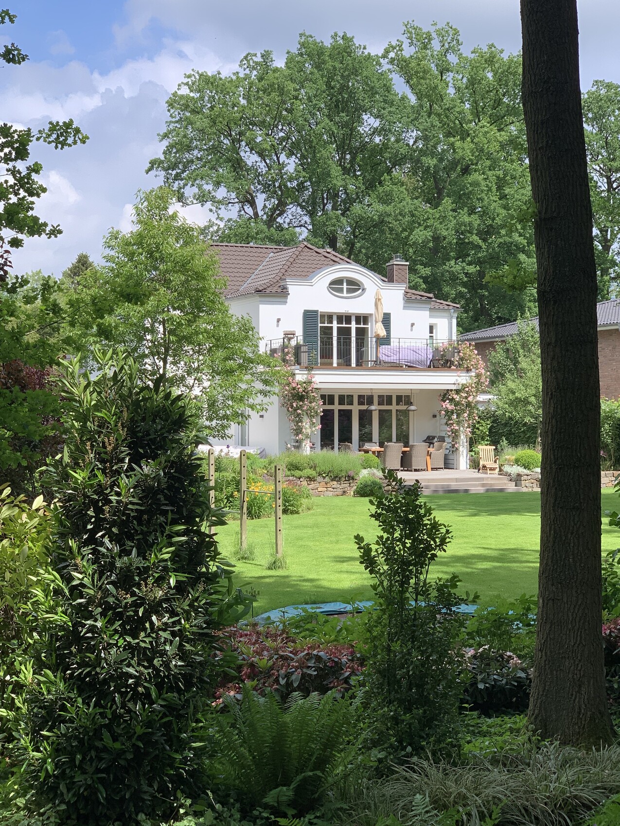Weiße zweistöckige Villa mit Balkon, Terrasse und grünem Garten im Vordergrund.