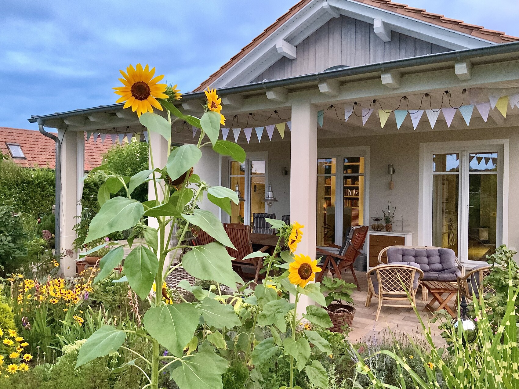Sonnenblumen im Vordergrund vor einer Veranda mit bunten Girlanden, Terrasse und Garten des Hauses.