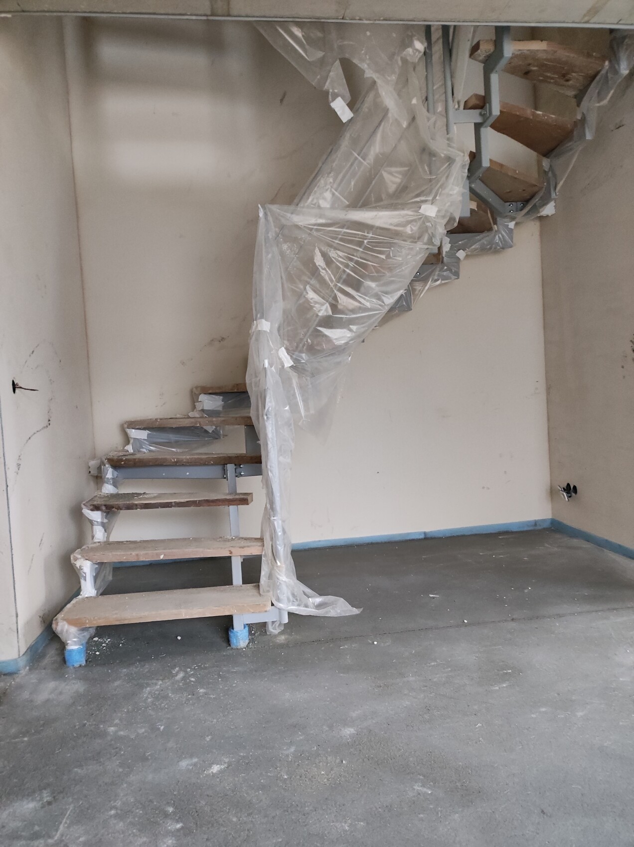 Spiralförmige Metalltreppe mit Holzstufen, provisorisch von Plastikfolie umhüllt.