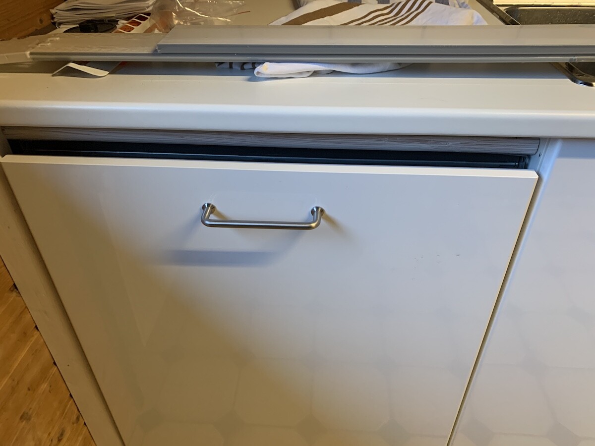 Weißer Geschirrspüler in der Küche mit Metallgriff; Stoffe liegen oben darauf.