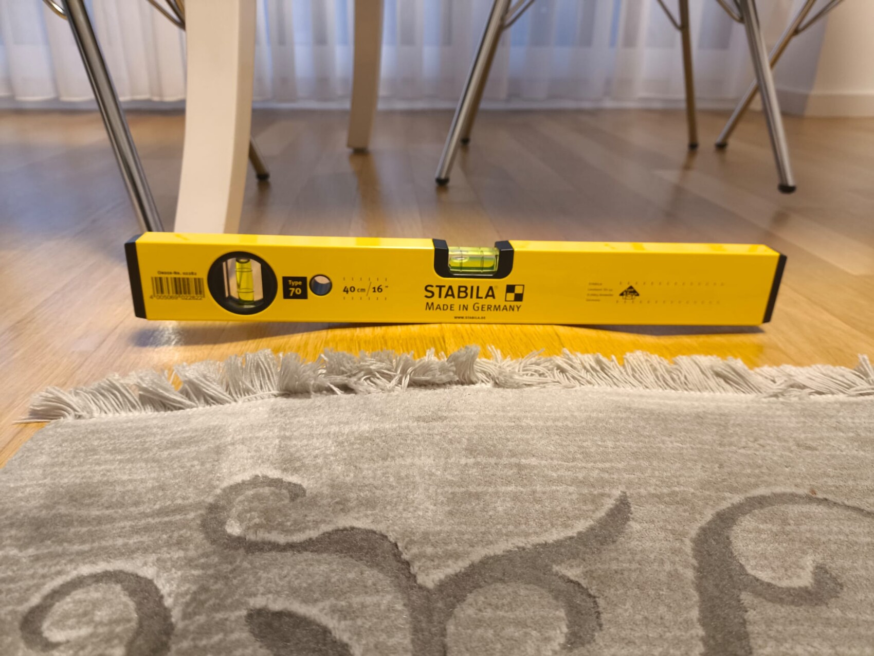 Gelbe STABILA-Wasserwaage liegt flach auf Holzfußboden neben Teppich und Tischbeinen.