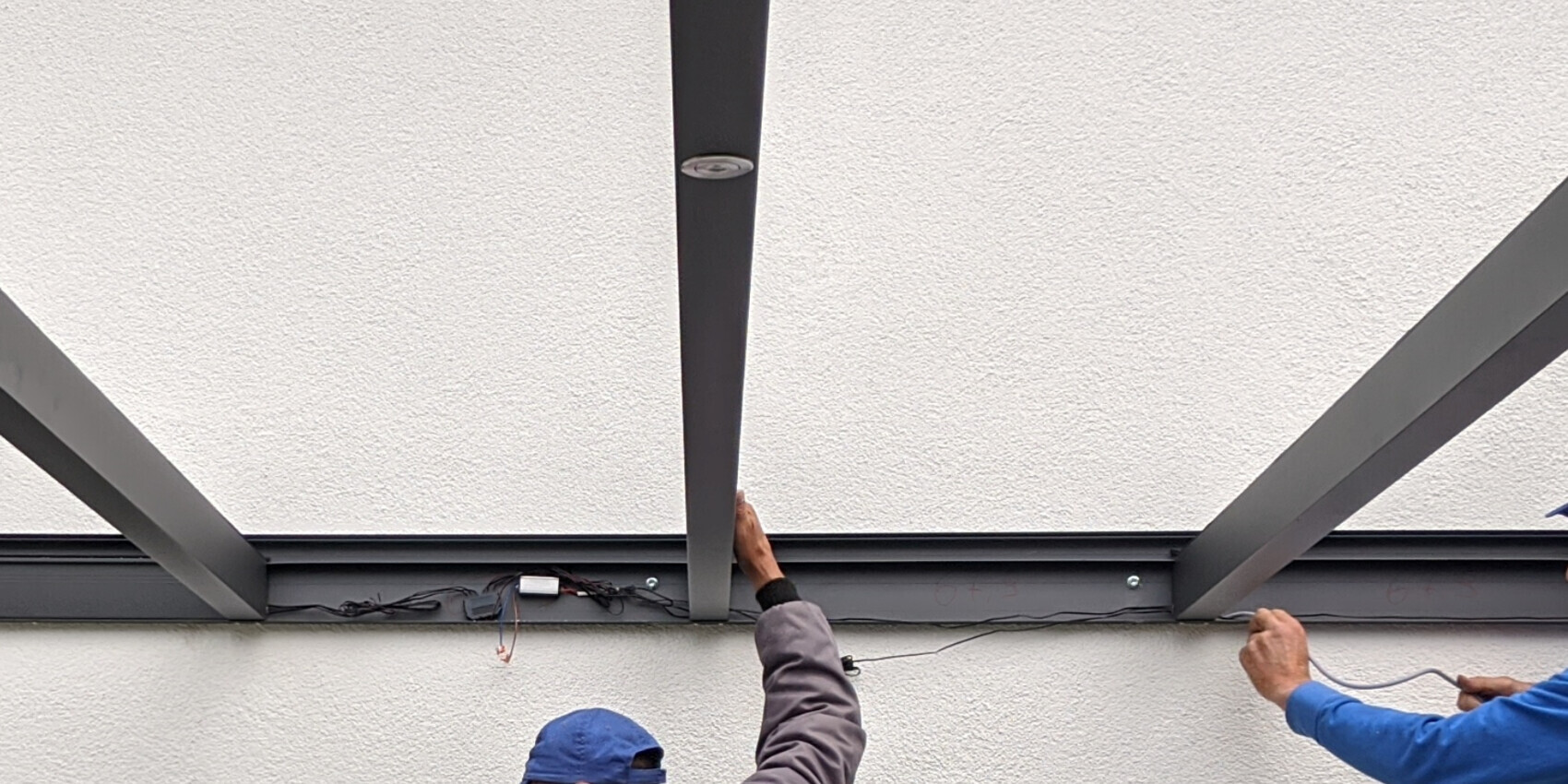 Mehrere Hände montieren eine Stahlträger-Konstruktion an der Decke, Kabel liegen herum.