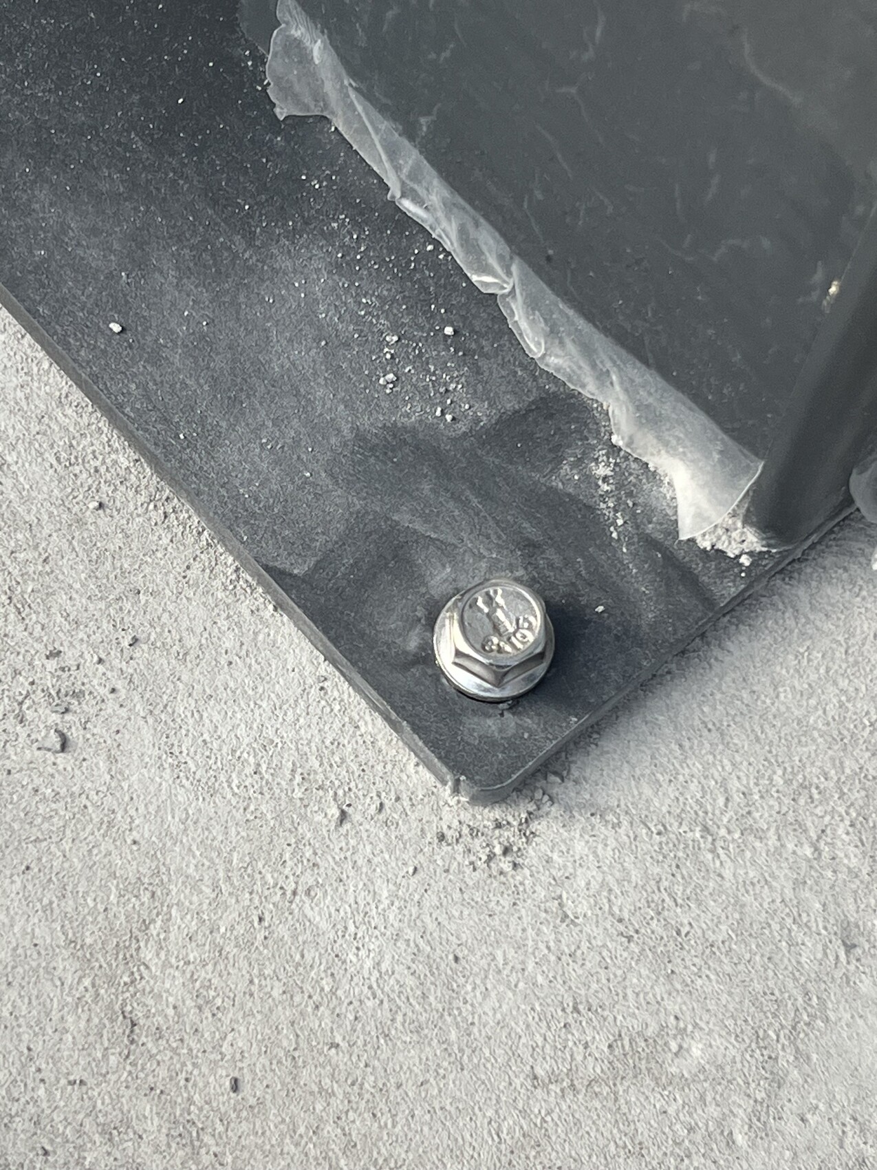 Nahaufnahme einer schwarzen Metallplatte mit Schraubbolzen auf Betonboden.