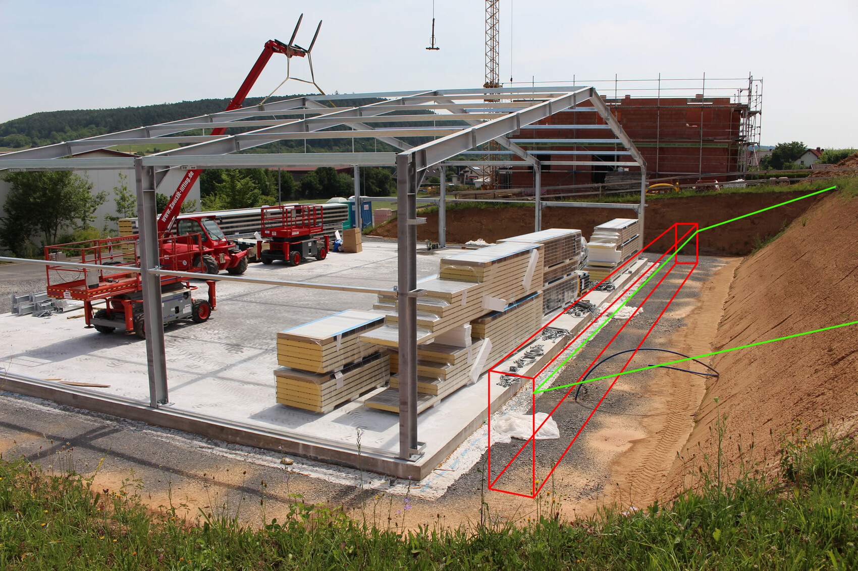 Baustelle mit Stahlrahmenkonstruktion, Kran, Baugerüst und Dämmplatten auf Betonfundament.