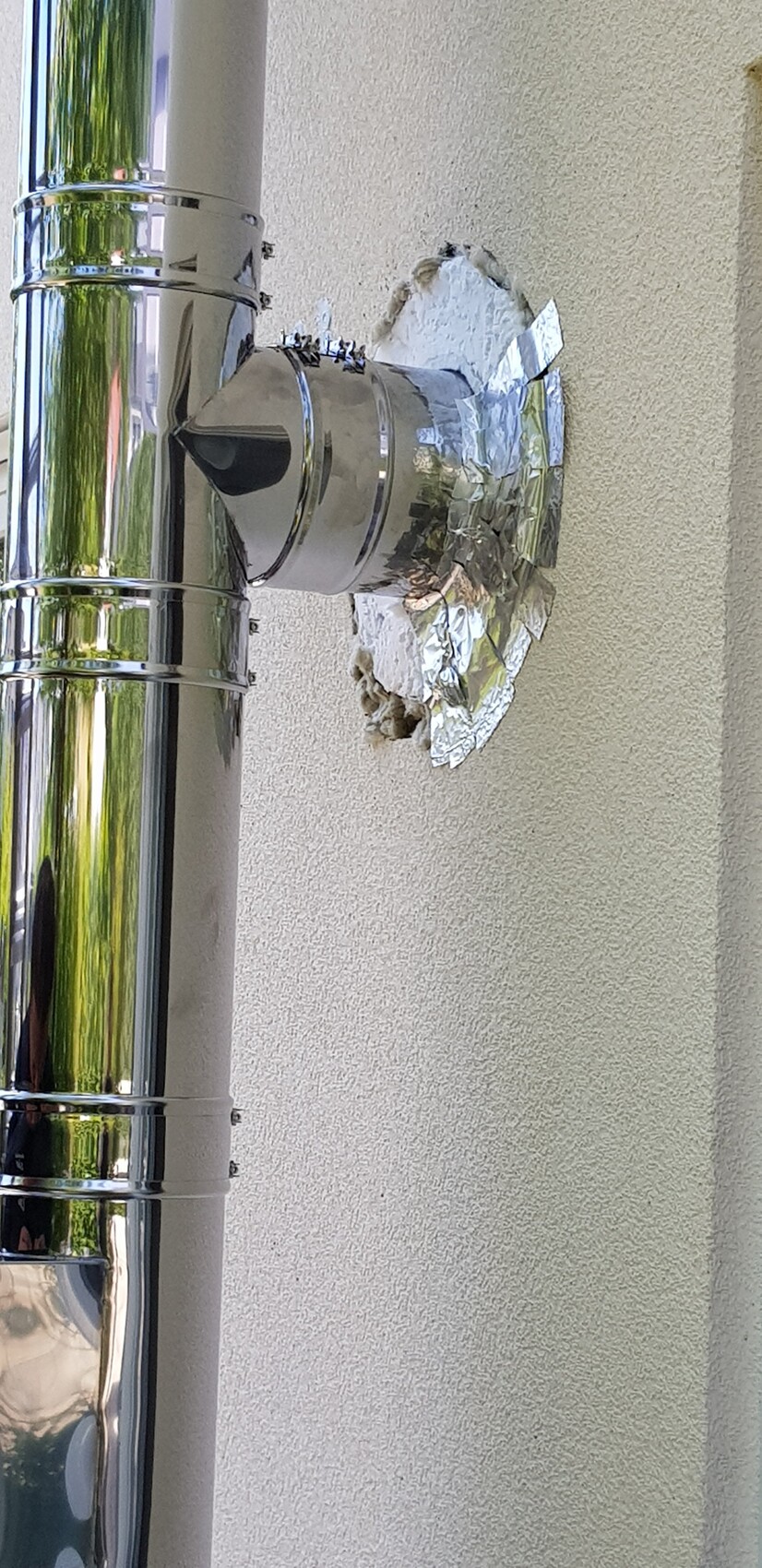 Außenwand mit silbernem Abgas-/Lüftungsrohr, Rundanschluss und Aluminiumfolie um die Öffnung.