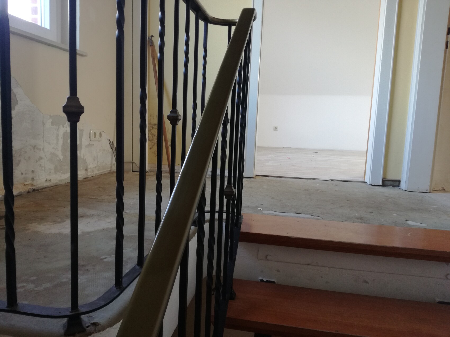 Innenraum einer renovierten Treppe mit schwarzem Metallgeländer, Holzstufen, offenes Zimmer.