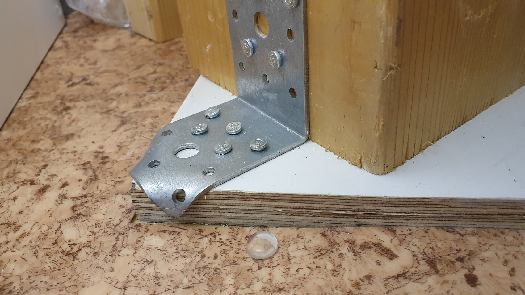 Metallwinkel-Verstärkung an Holzpfosten, Schrauben sichtbar, Bodenplatte aus Holz.