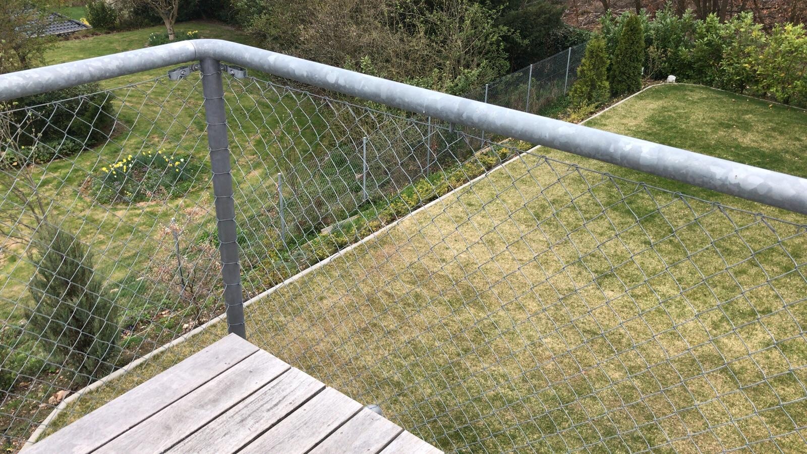 Blick von einer Holzterrasse auf einen Garten mit Drahtzaun und Rasen.